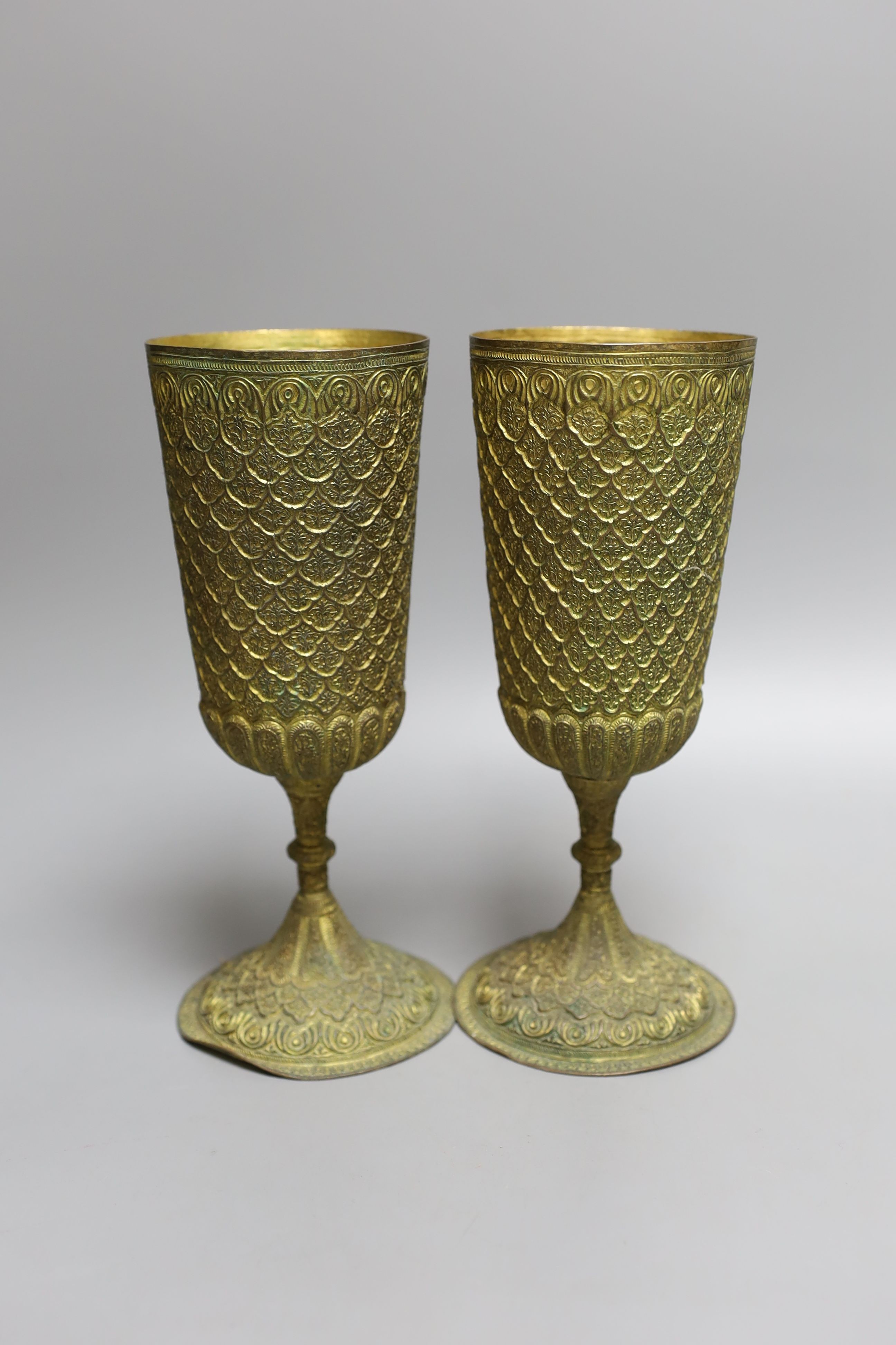 A pair of Middle Eastern repousse gilt metal goblets, 22cms high.
